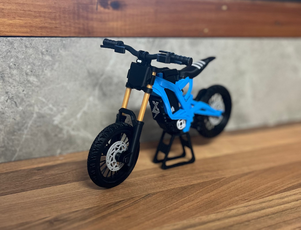 Small blue and black toy dirt bike on a wooden surface with a blurred background