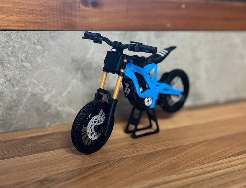 Small blue and black toy dirt bike on a wooden surface with a blurred background